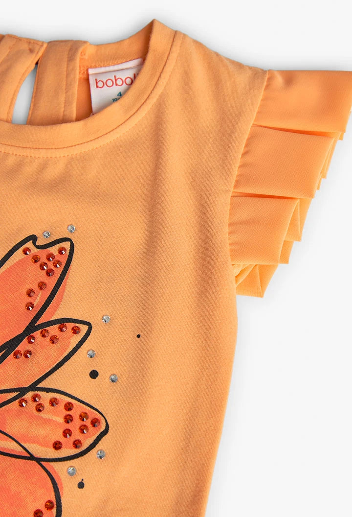 Detalle superior de blusa naranja Boboli con flor ilustrada, aplicaciones brillantes y mangas plisadas.