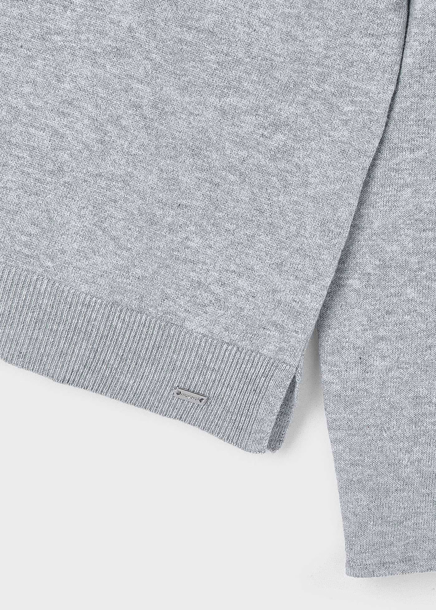 Detalle del bajo y la abertura lateral de un suéter de punto fino color gris, con una placa metálica de la marca Mayoral.