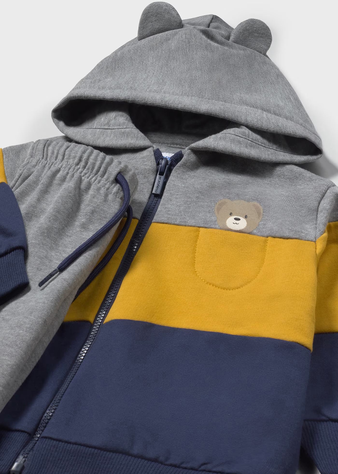 Detalle del bolsillo con un osito bordado y la capucha con orejitas de una sudadera con cremallera, marca Mayoral.