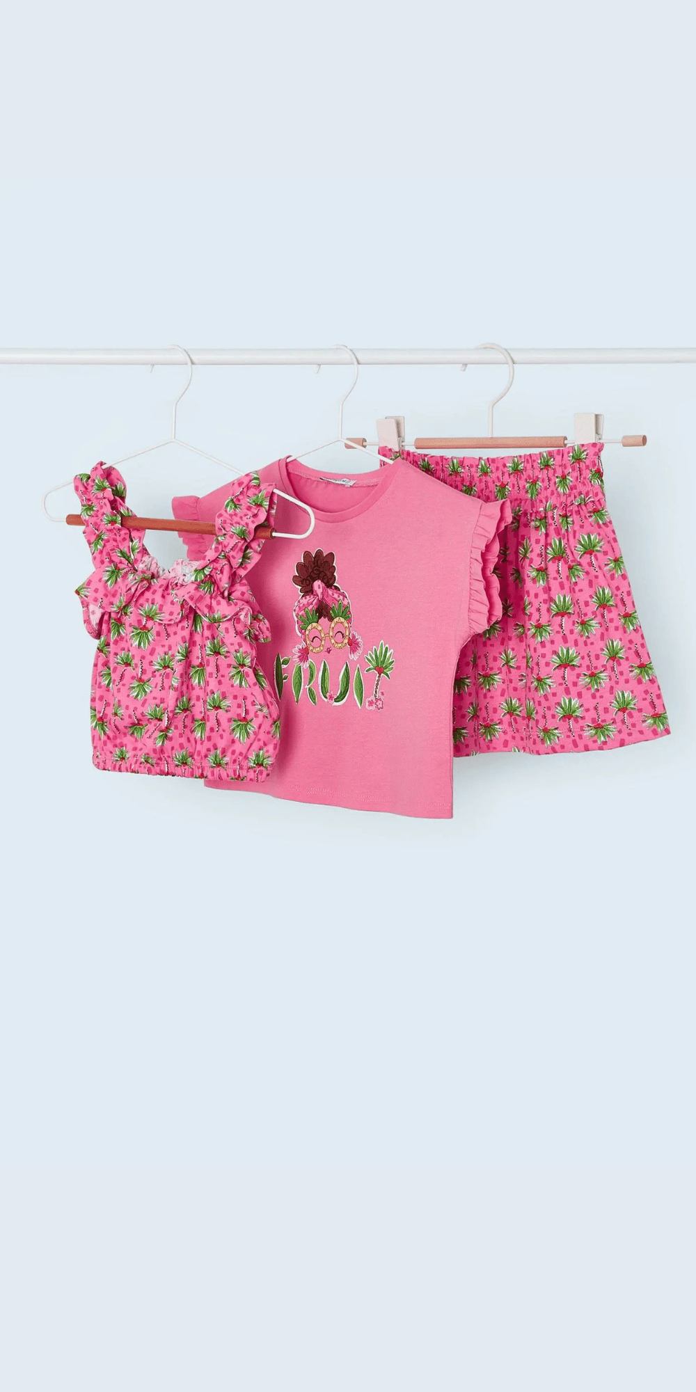 Conjunto de verano para niña en tonos rosas con estampado tropical de frutas. Incluye una blusa sin mangas con volantes, una camiseta de manga corta con diseño de frutas y una falda estampada. Perfecto para los días soleados con un estilo fresco y divertido.