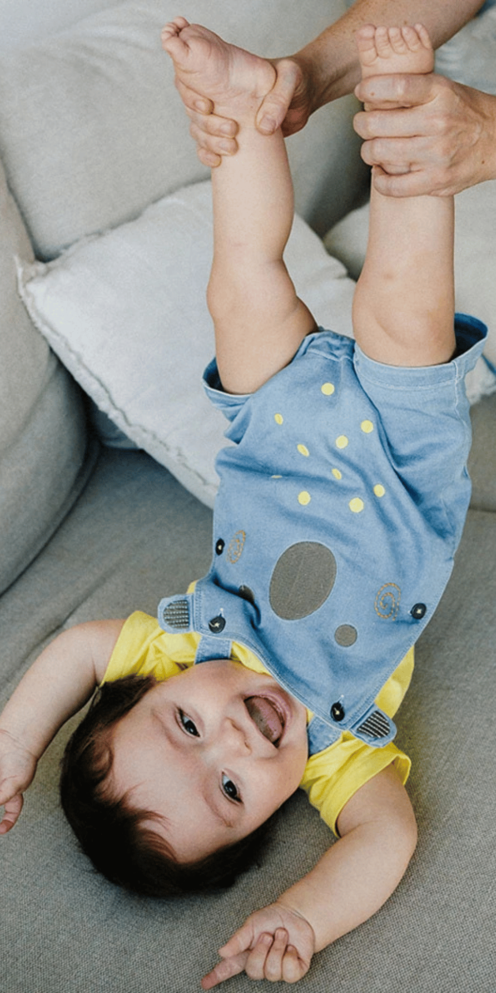 Bebé feliz jugando en un sofá con conjunto amarillo y overol de mezclilla azul con diseño de koala.