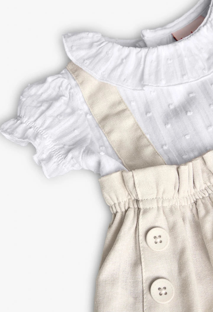 Detalle de la blusa blanca con cuello fruncido y mangas cortas, con tirantes de lino beige y botones en la parte delantera.