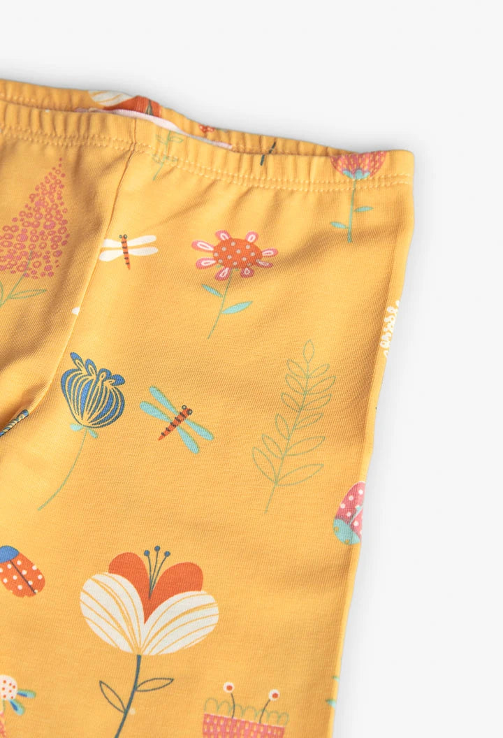 Detalle de la tela de los leggings amarillos con diseño de flores y mariposas coloridas.