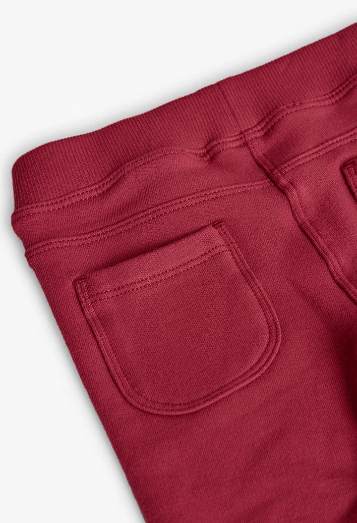 Detalle del bolsillo trasero de parche y la cintura elástica de unos jeggings de felpa color guinda.