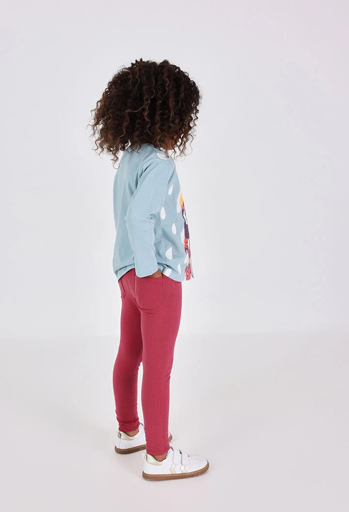 Vista trasera de una niña usando jeggings color guinda, mostrando los bolsillos traseros.