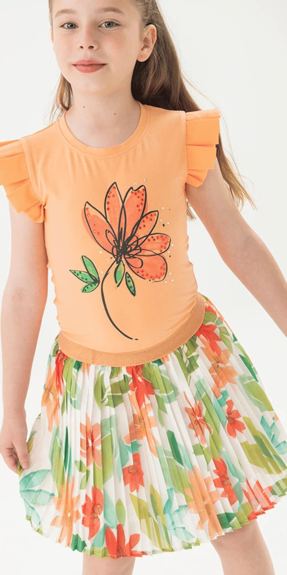 Niña usando conjunto floral Boboli con blusa naranja ilustrada y falda plisada estampada, ideal para un look alegre y mágico.