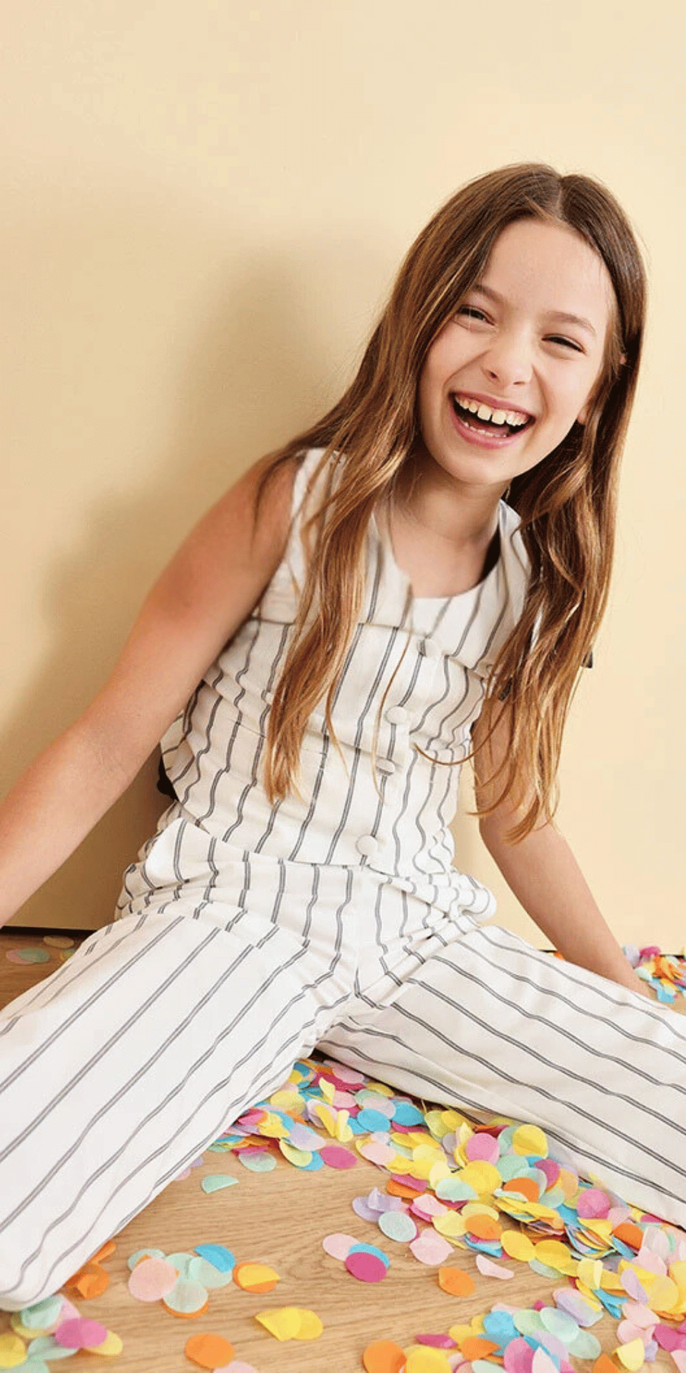 Niña sonriente usando conjunto rayado blanco con negro de Boboli, sentada sobre confeti de colores.