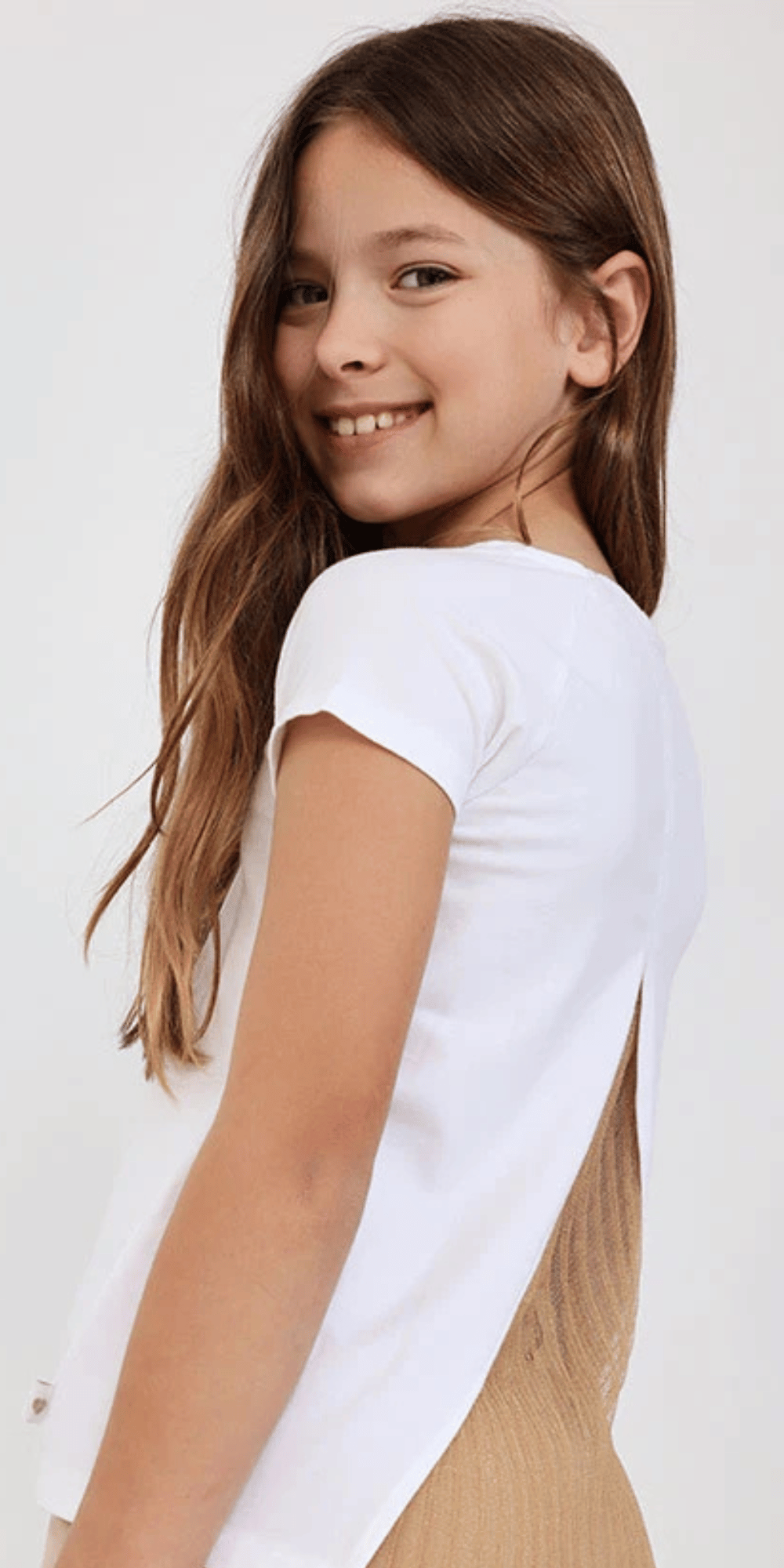 Niña de espaldas usando playera blanca Boboli con abertura posterior y falda plisada metálica.