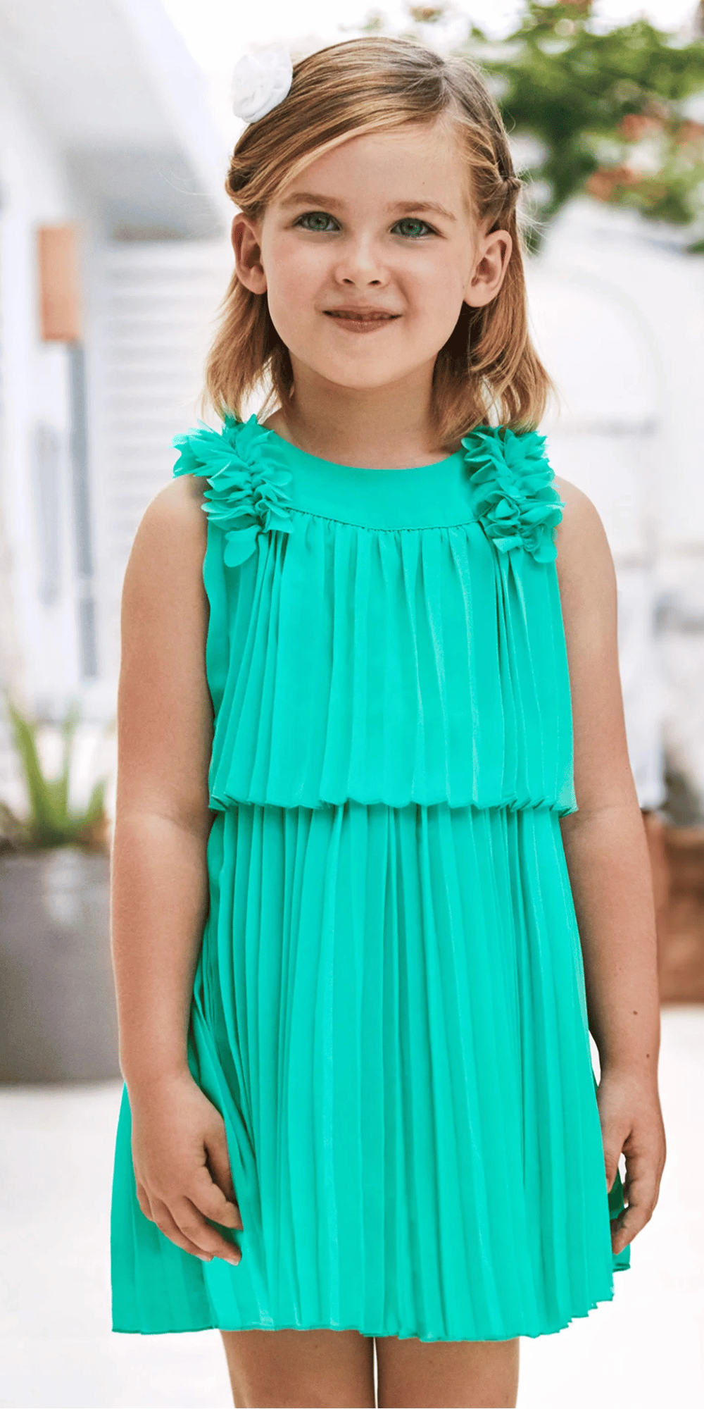 Niña usando un elegante vestido plisado en color verde vibrante con detalles florales en los hombros. Diseño sin mangas ideal para eventos especiales y ocasiones formales.