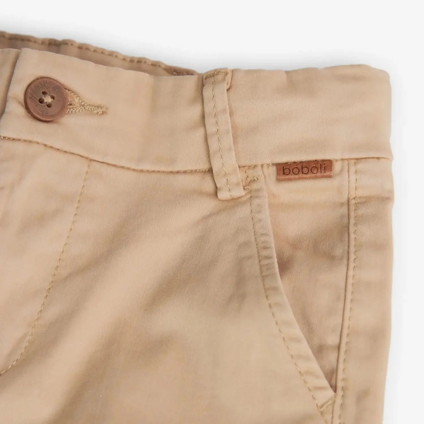 Detalle frontal del pantalón beige Boboli de Cachaboo, con botón de madera, bolsillos laterales y etiqueta decorativa de la marca.