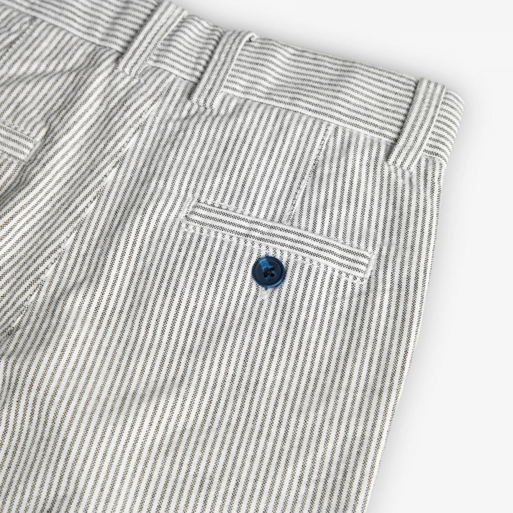 Bolsillo trasero con botón azul del pantalón de rayas blancas y grises para niño, con diseño clásico y acabado elegante.