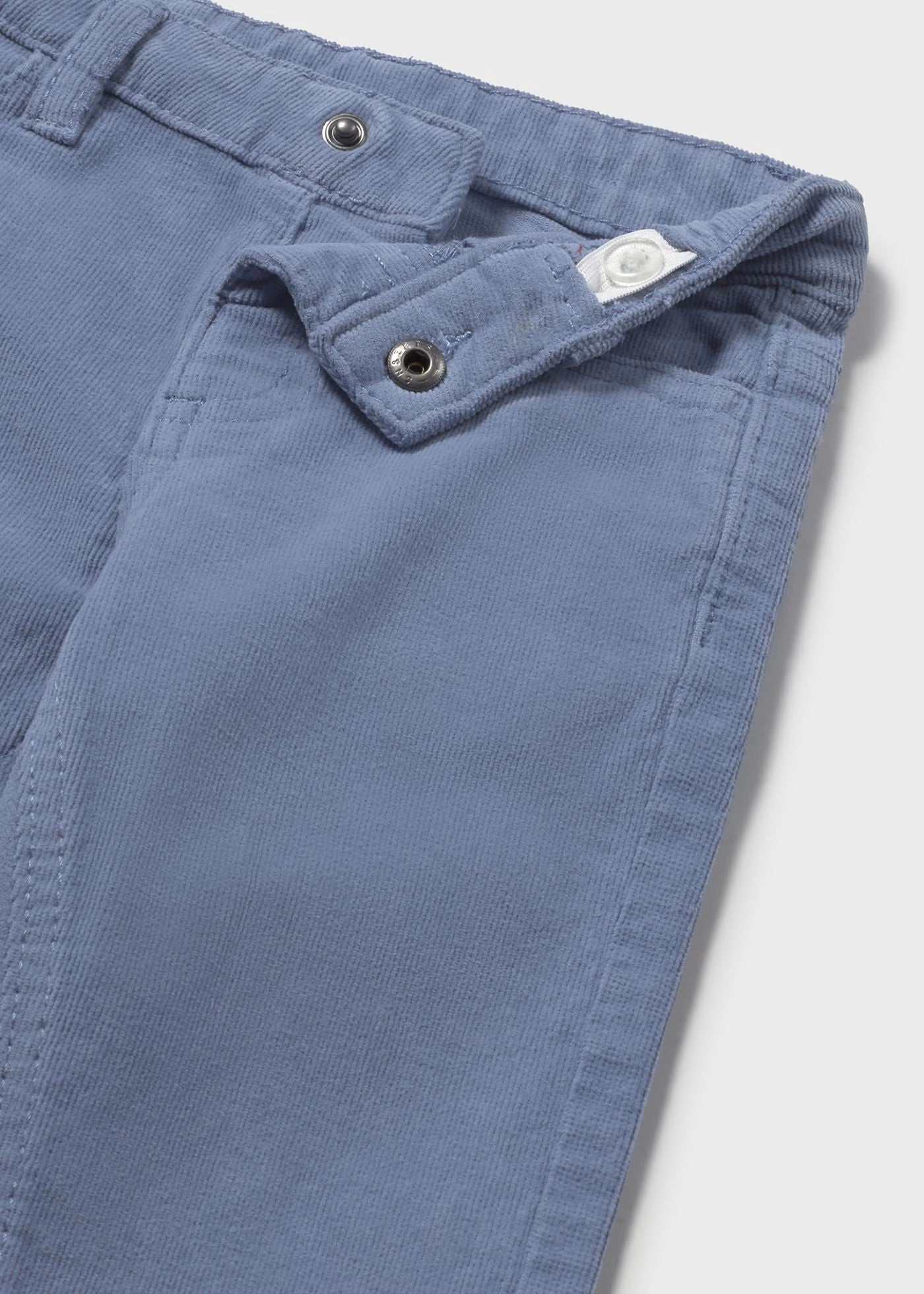 Detalle del botón y la cintura interior ajustable de un pantalón de pana azul para niño.