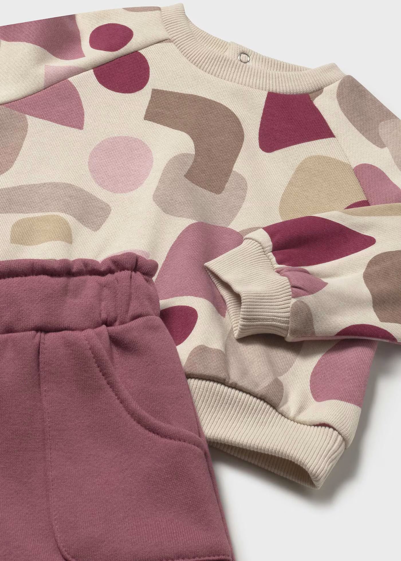 Detalle de un conjunto de felpa, mostrando el estampado de la sudadera, el puño y la cintura elástica del pantalón.