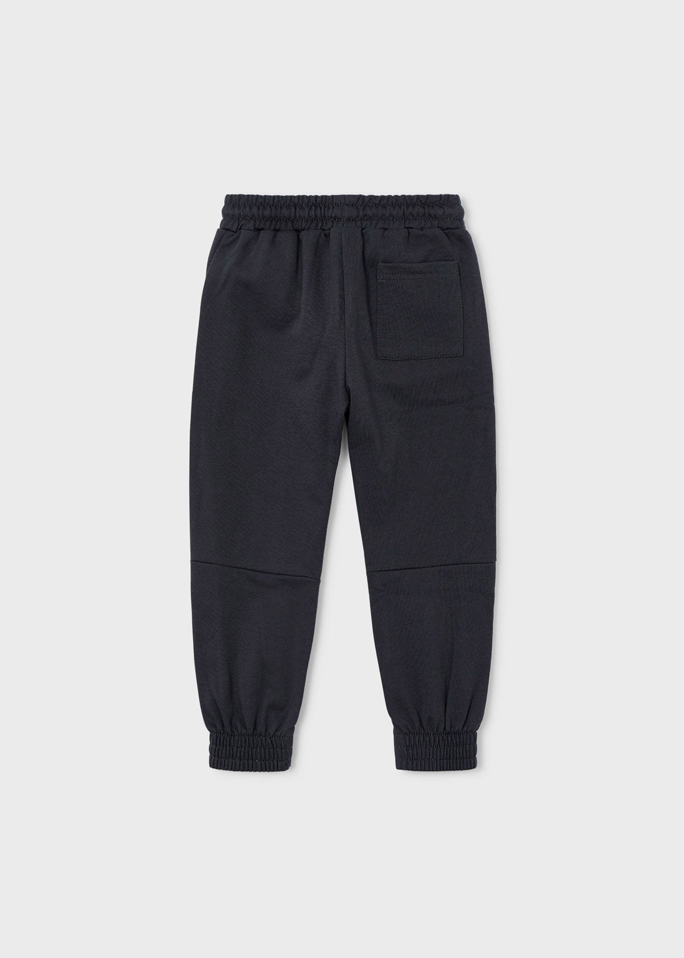 Vista trasera de un pantalón jogger de felpa color gris oscuro para niño, con paneles en las rodillas.