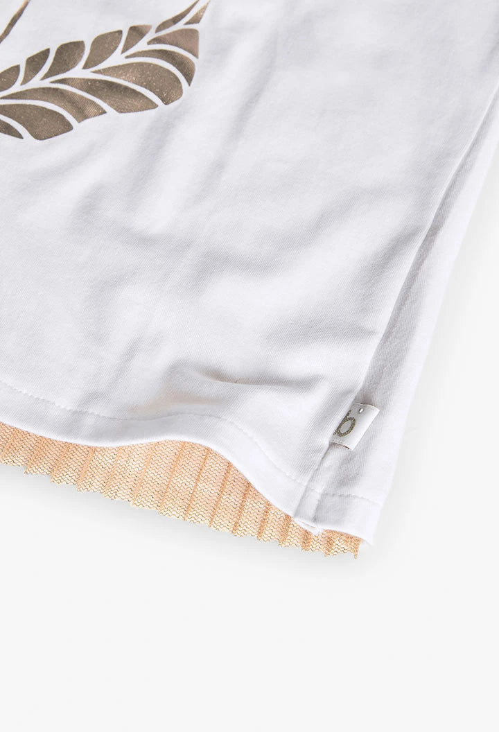 Detalle del dobladillo de playera blanca con estampado floral en dorado y etiqueta lateral.
