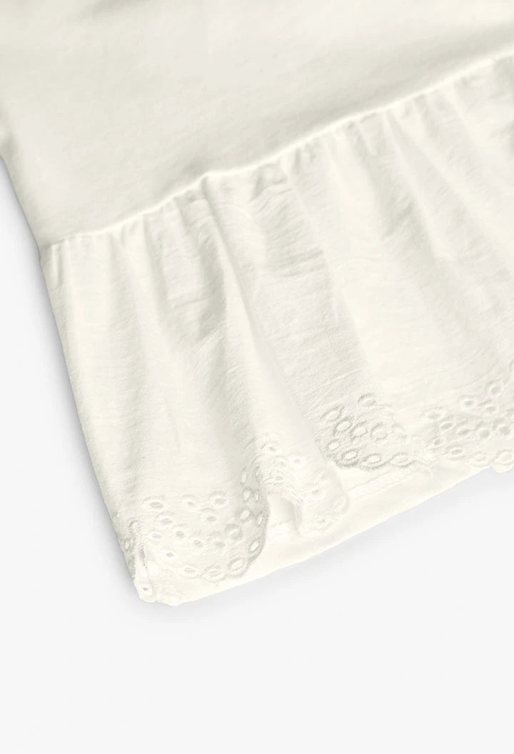 Detalle del volante bordado en el dobladillo de la playera blanca de manga larga.