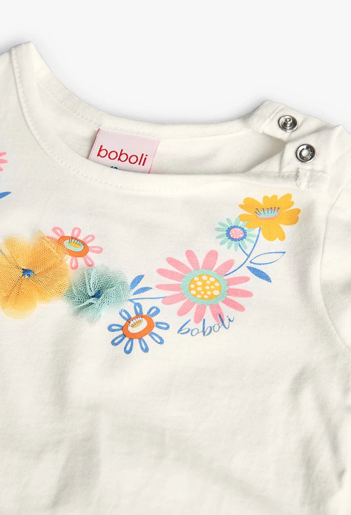 Detalle del cuello de una playera blanca de manga larga con flores bordadas y aplicaciones en relieve de tul en tonos pastel. Botones de presión en el hombro para facilitar el ajuste.
