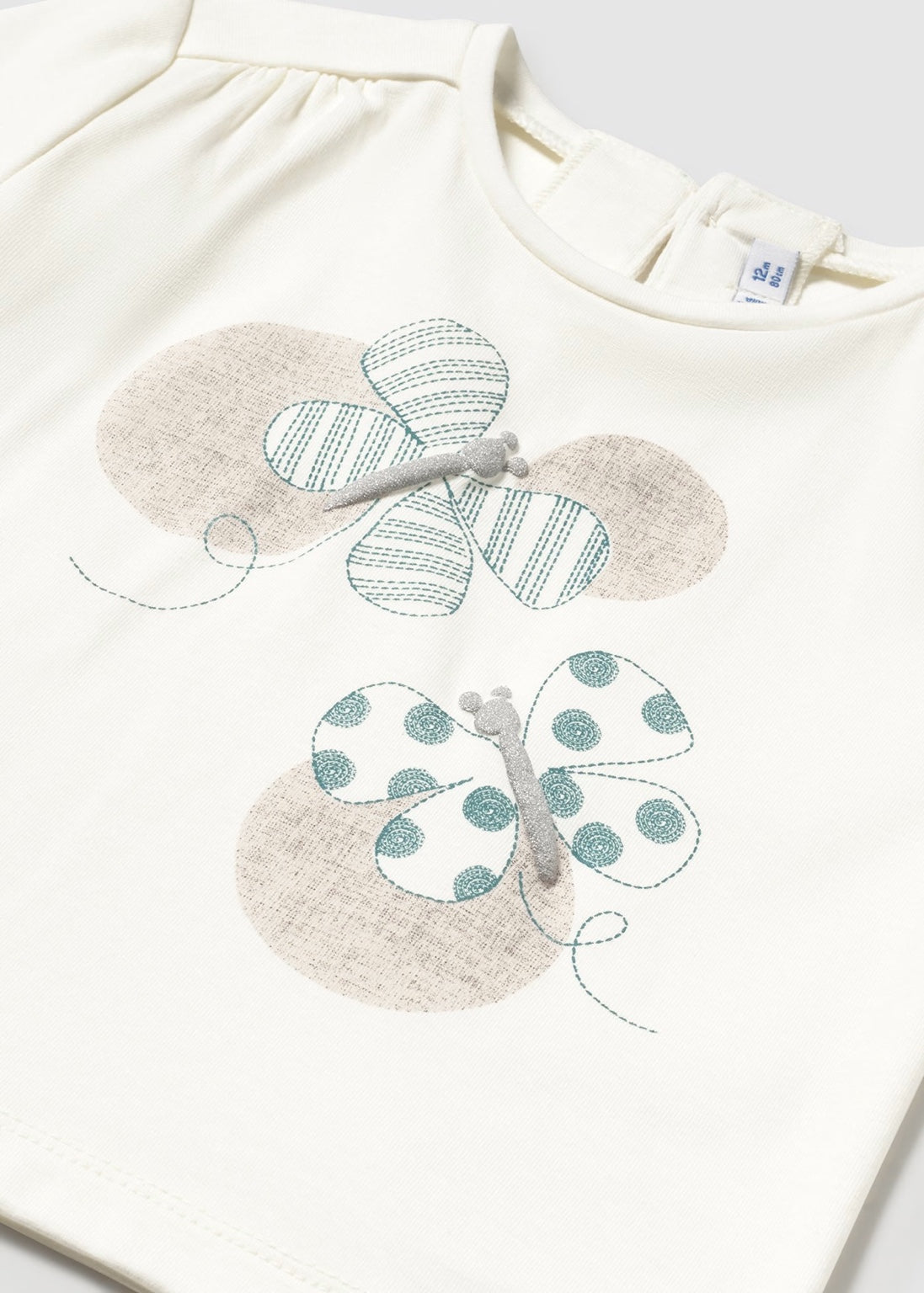 Detalle del estampado de mariposas en tonos pastel de la playera en color hueso de Mayoral.