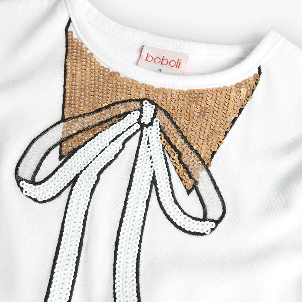 Primer plano del moño de lentejuelas doradas en la playera blanca Boboli para niña