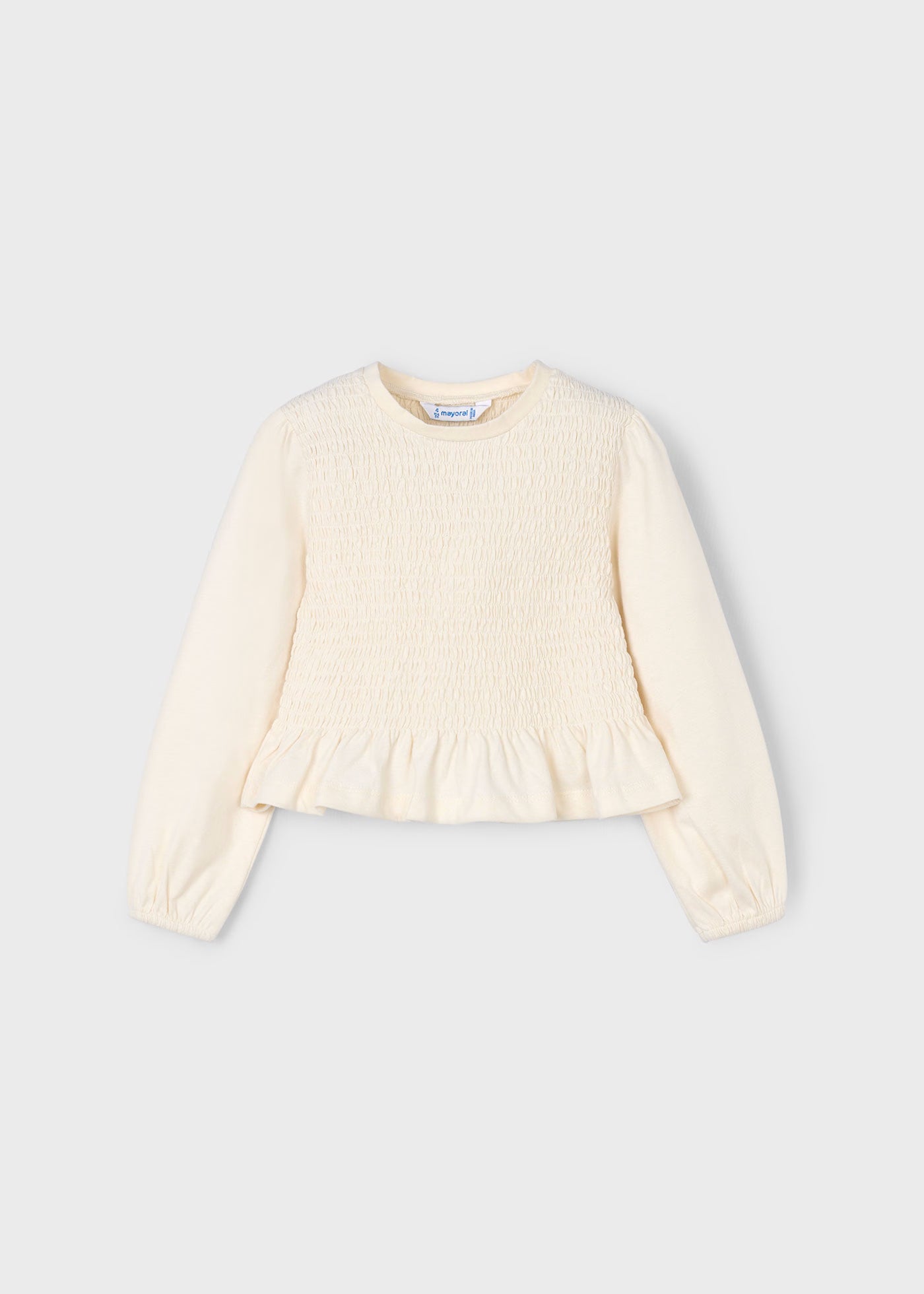 Vista frontal de una blusa de manga larga para niña en color crudo, con cuerpo elástico de nido de abeja y volante.