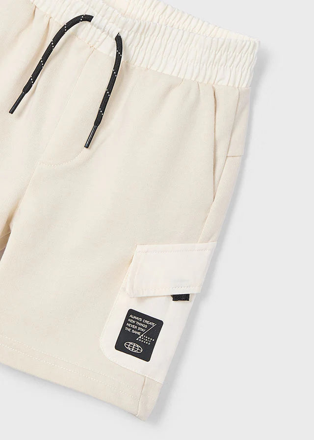 Detalle de shorts beige Mayoral con bolsillo lateral y etiqueta con mensaje de diseño urbano.