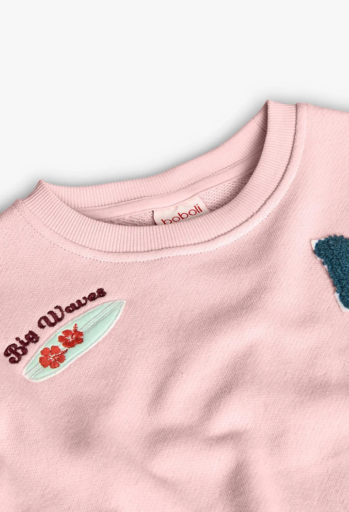 Detalle del cuello redondo y parche de tabla de surf con flores en sudadera rosa.