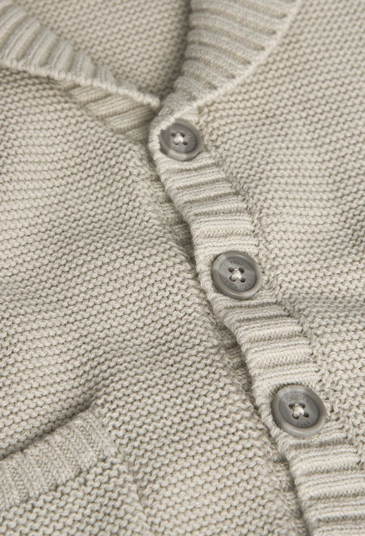 Primer plano de un suéter beige tejido con botones, resaltando la textura y los detalles de su confección.