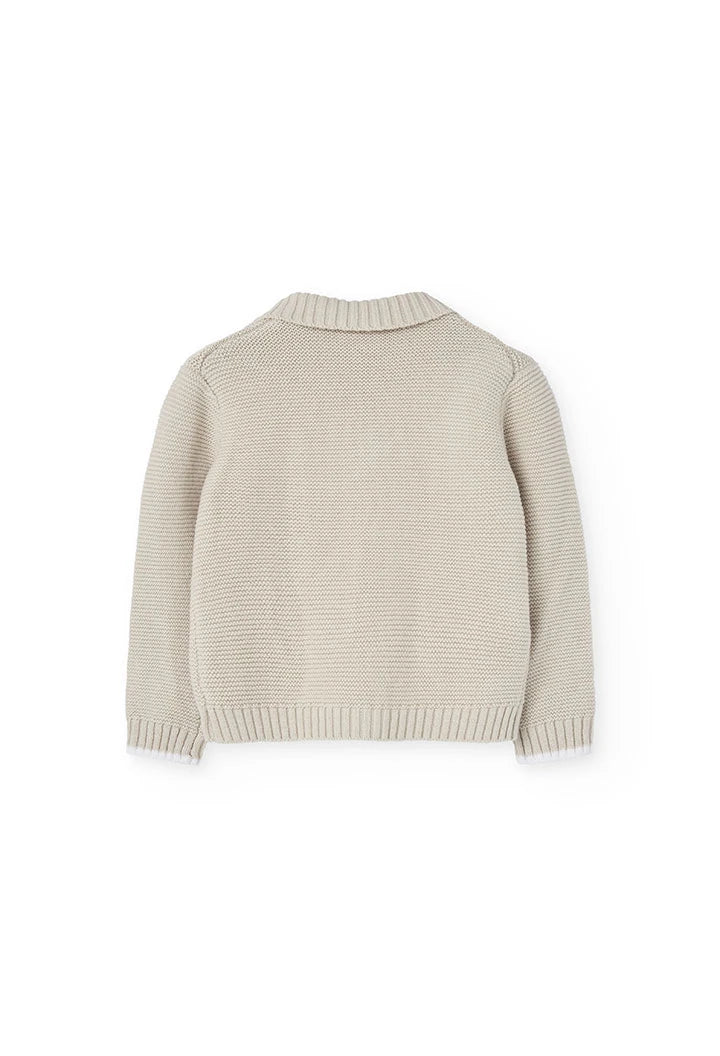 Vista trasera de un suéter beige tejido para niños, con un diseño clásico y cuello tipo chal.