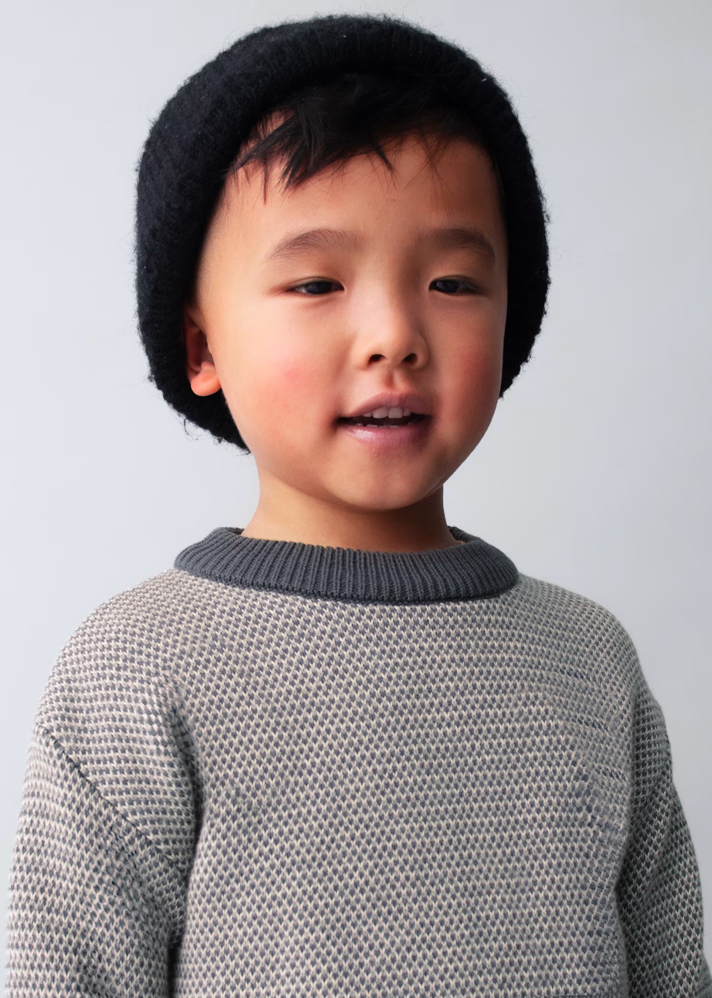 Primer plano de un niño usando un suéter de punto con textura bicolor y cuello a contraste, marca Mayoral.