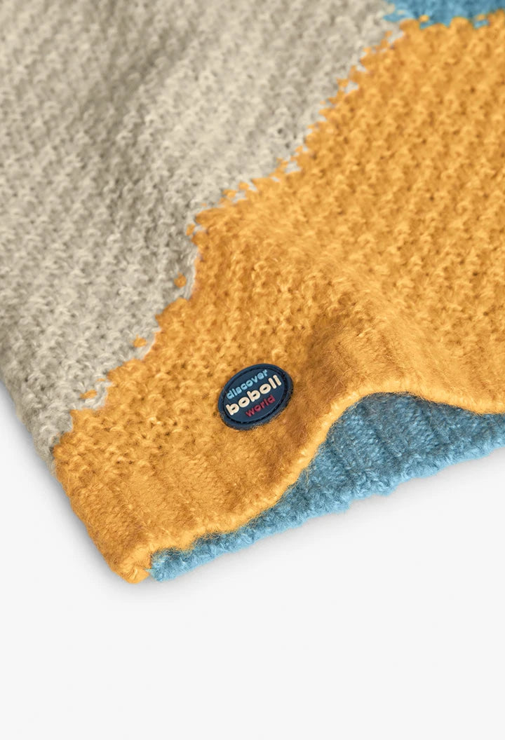 Detalle del parche azul de la marca "discover boboli world" en el bajo de un suéter de punto con bloques de color.