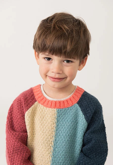 Primer plano del rostro de un niño usando un suéter de punto con bloques de colores y cuello contrastante color coral, marca Boboli.
