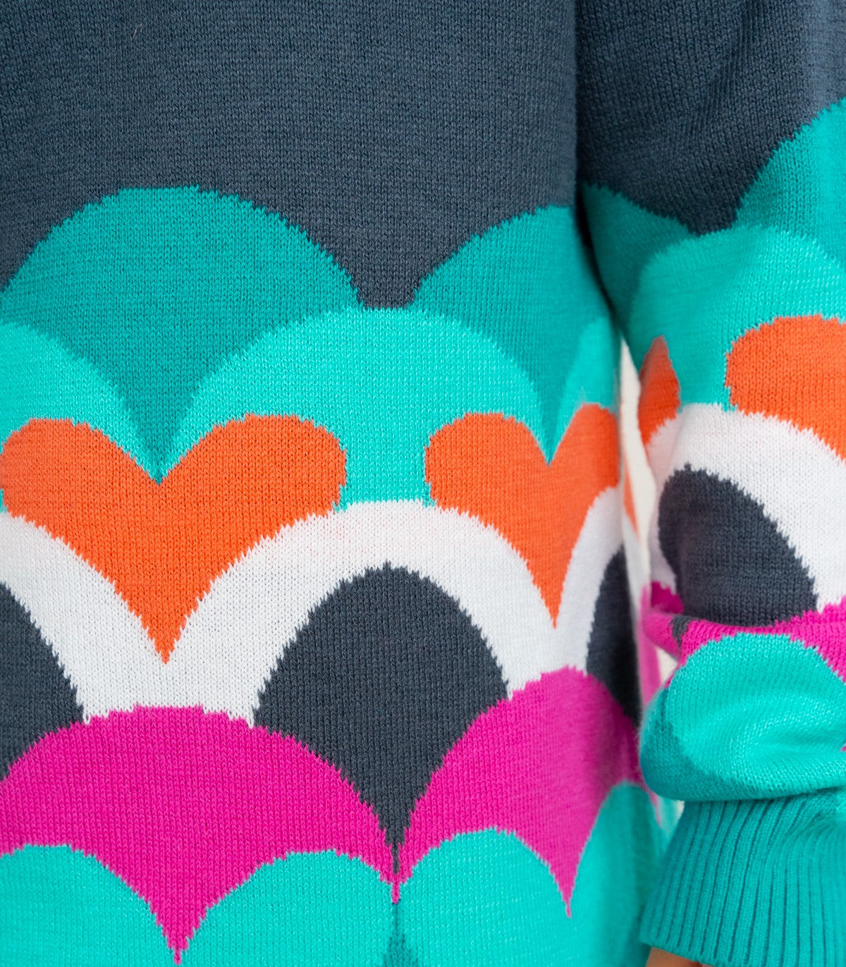 Detalle de las mangas del vestido Boboli con corazones tejidos en tonos aqua, rosa y naranja.