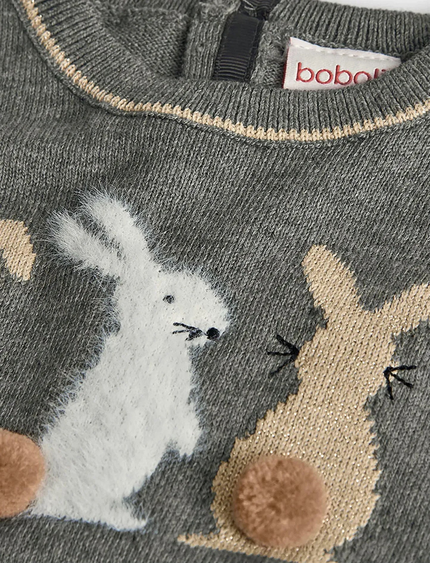 Detalle del aplique de conejitos en un suéter gris, mostrando un conejo blanco afelpado, uno dorado brillante y colas de pompón, marca Boboli.