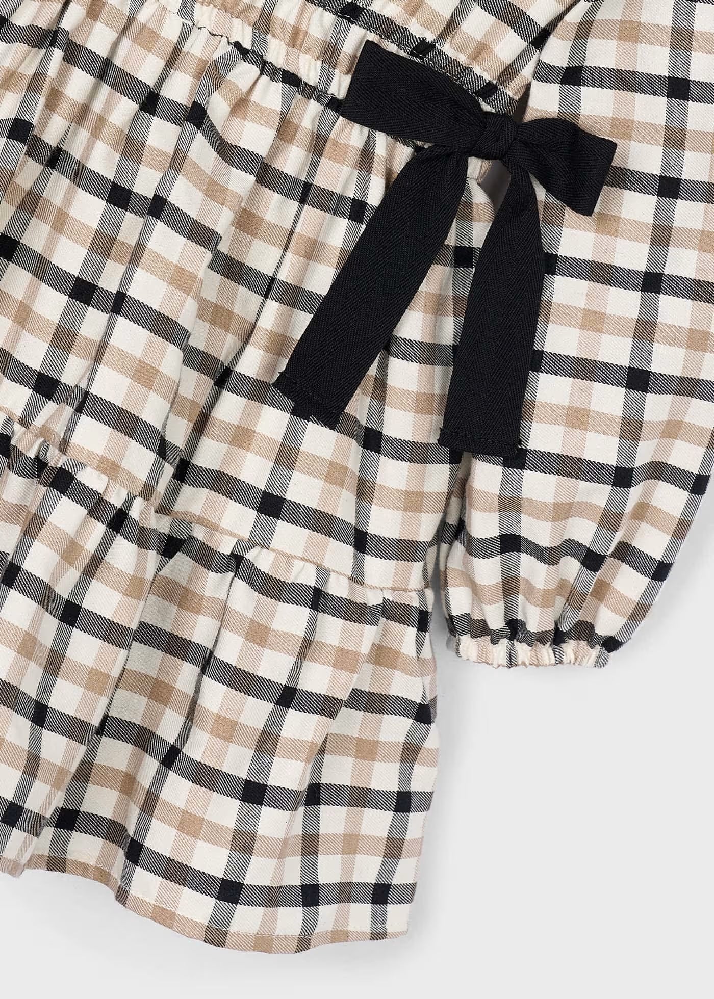 Detalle de uno de los moños negros y el volante en la falda de un vestido de sarga a cuadros, marca Mayoral.
