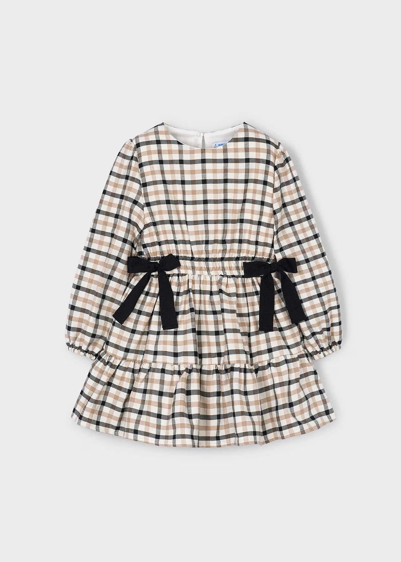 Vista frontal de un vestido de manga larga para niña con estampado de cuadros, cintura elástica, dos moños negros y falda con volante, marca Mayoral.