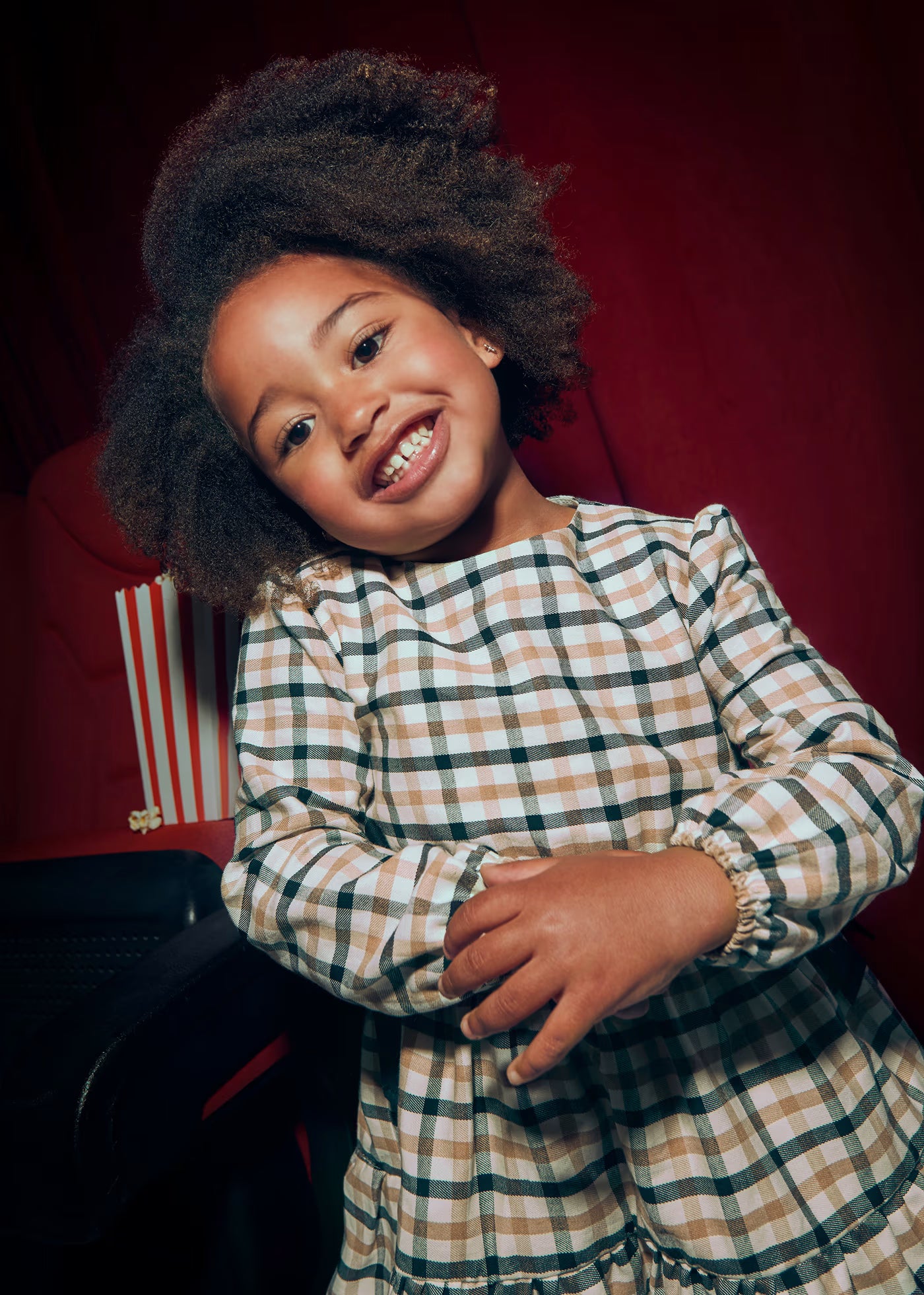 Primer plano de una niña sonriendo, usando un vestido de manga larga a cuadros en tonos neutros, marca Mayoral.