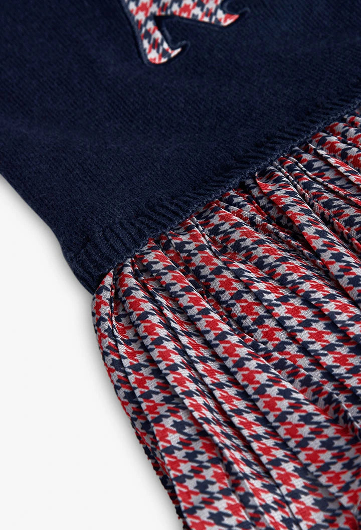 Primer plano de la unión entre el suéter de punto azul y la falda plisada con estampado de pata de gallo, marca Boboli.