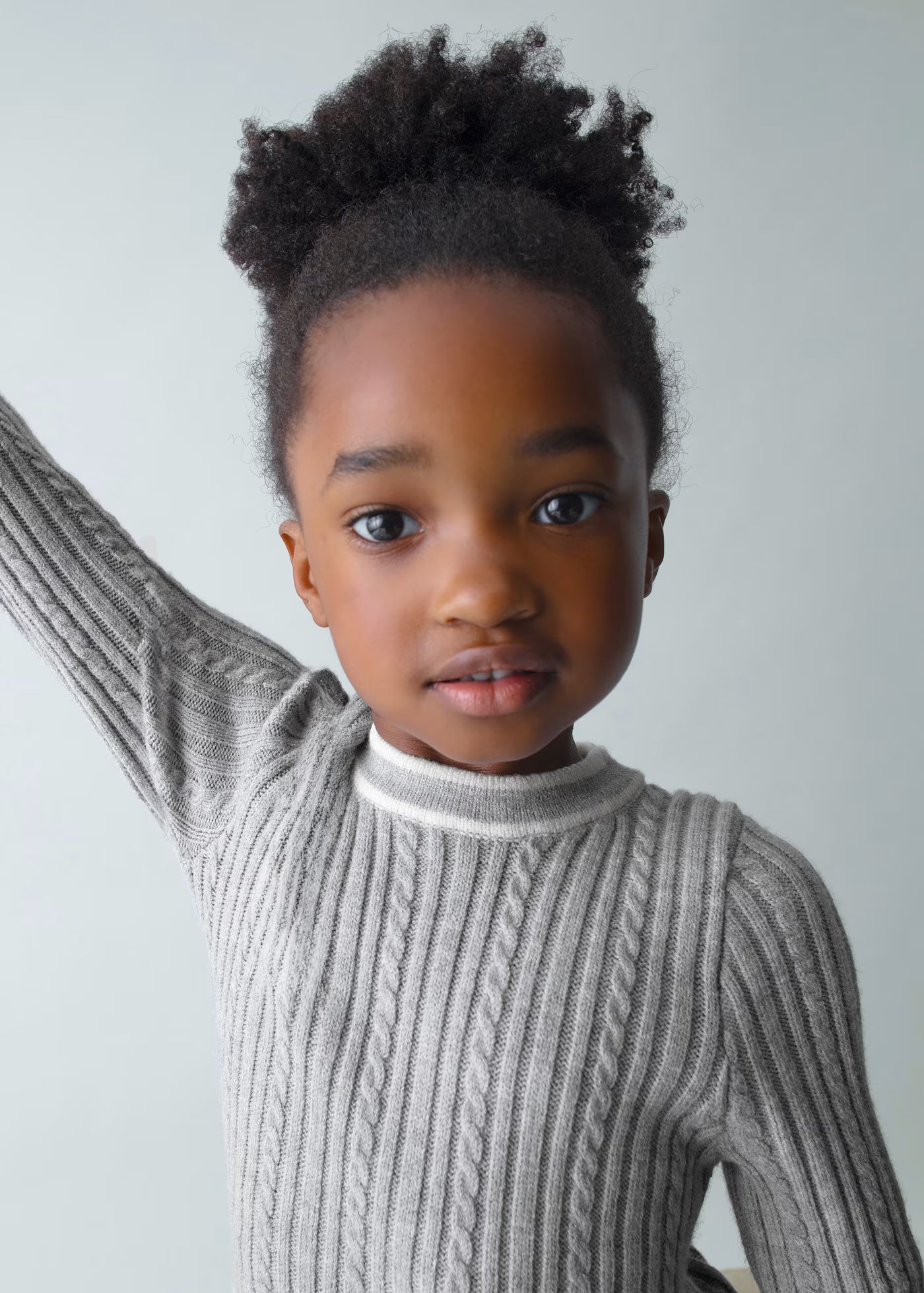 Primer plano del rostro de una niña usando un vestido de punto trenzado gris con cuello a contraste, marca Mayoral.