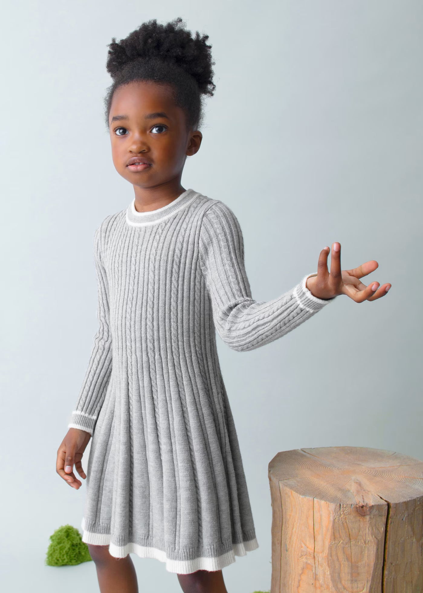 Niña posando de pie con un vestido de punto gris de corte evasé y manga larga, marca Mayoral.
