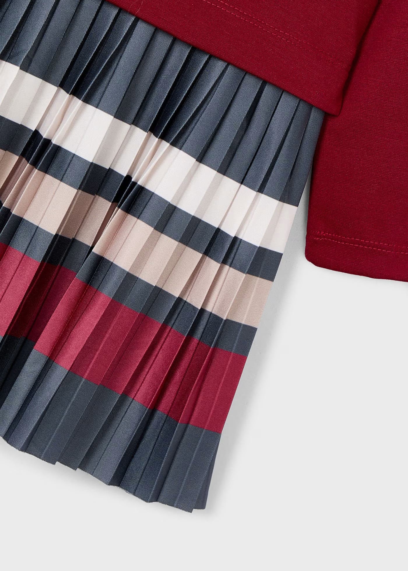 Detalle de la falda plisada de un vestido, mostrando las rayas horizontales en colores gris, vino, crudo y beige.