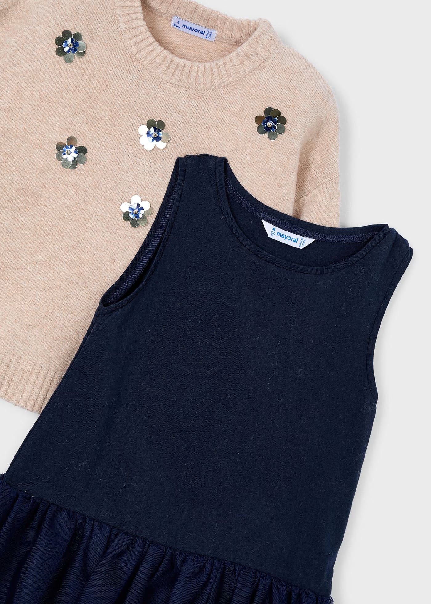 Detalle de un conjunto para niña, mostrando las flores de lentejuelas en el suéter de punto y el vestido de tul azul marino debajo, marca Mayoral.
