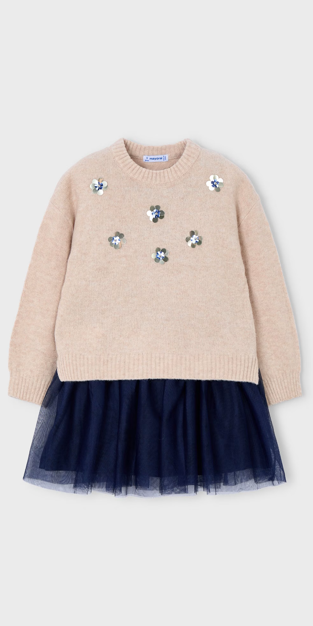 Vista frontal de un conjunto de dos piezas para niña: un suéter de punto color avena con flores de lentejuelas sobre un vestido con falda de tul azul marino, marca Mayoral.