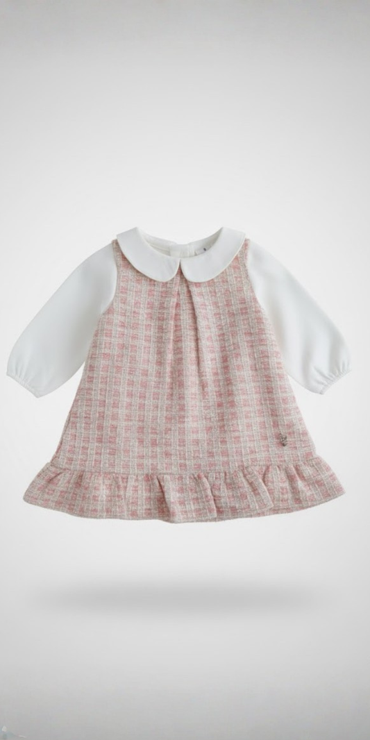 Vista frontal de un vestido para bebé estilo "jumper", con cuerpo de tweed rosa, blusa blanca integrada con cuello Peter Pan y un volante en el bajo.