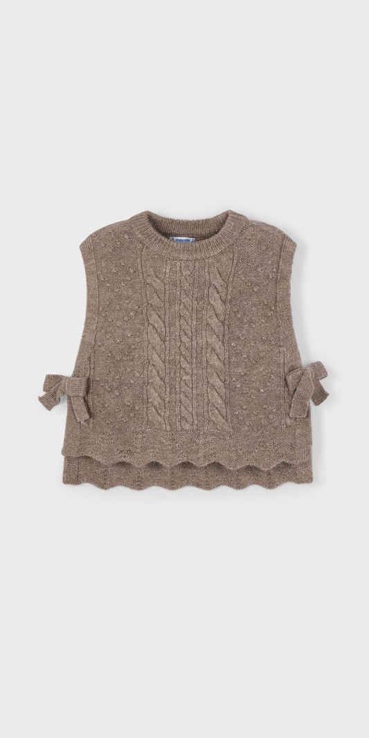 Vista frontal de un chaleco de punto para niña en color topo, con textura trenzada, bajo ondulado y moños en los costados, marca Mayoral.