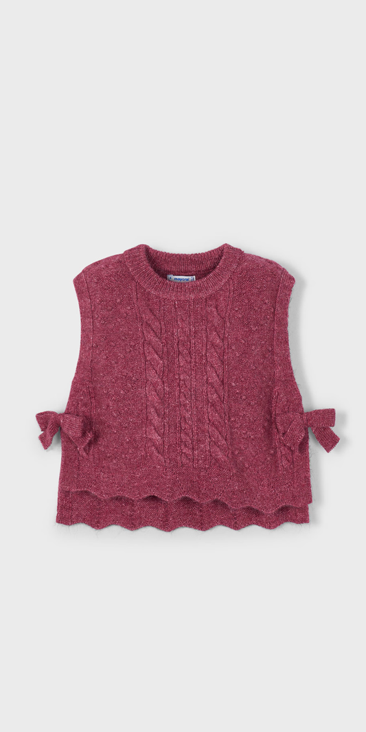 Vista frontal de un chaleco de punto para niña en color cereza, con textura trenzada, bajo ondulado y moños en los costados, marca Mayoral.