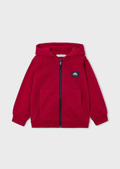 Vista frontal de una sudadera roja con capucha, cremallera y un parche de dinosaurio en el pecho, marca Mayoral.