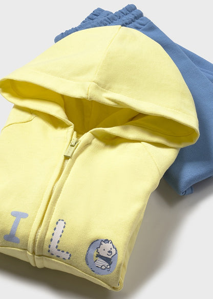 Primer plano de una sudadera con capucha en color amarillo neón con cierre frontal y detalles bordados, acompañada de un pantalón azul con cintura elástica, ideal para bebés o niños pequeños.

