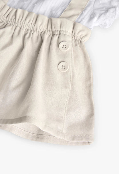 Primer plano del vestido de lino beige para bebé con botones decorativos en la falda y elástico en la cintura.