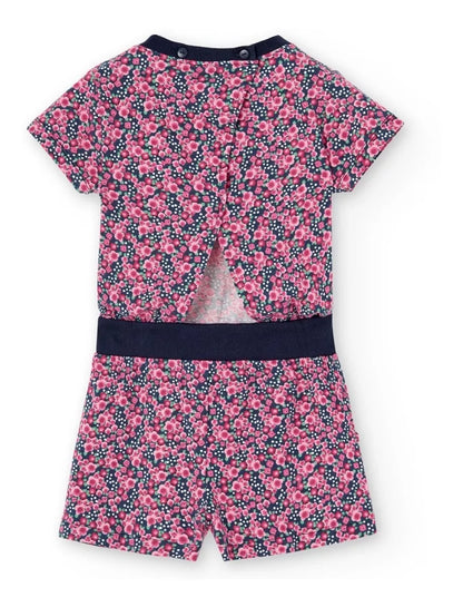 Vista trasera del jumpsuit corto de Boboli con estampado floral en tonos rosas sobre fondo azul marino. Diseño de manga corta con abertura en la espalda y cierre con botones en el cuello. Cintura elástica con banda azul y bolsillos laterales.