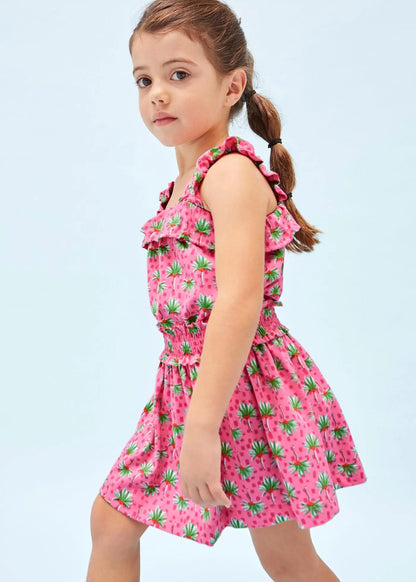 Niña vistiendo un hermoso vestido rosa con estampado tropical de frutas y tirantes con volantes. Ideal para días soleados y actividades al aire libre.